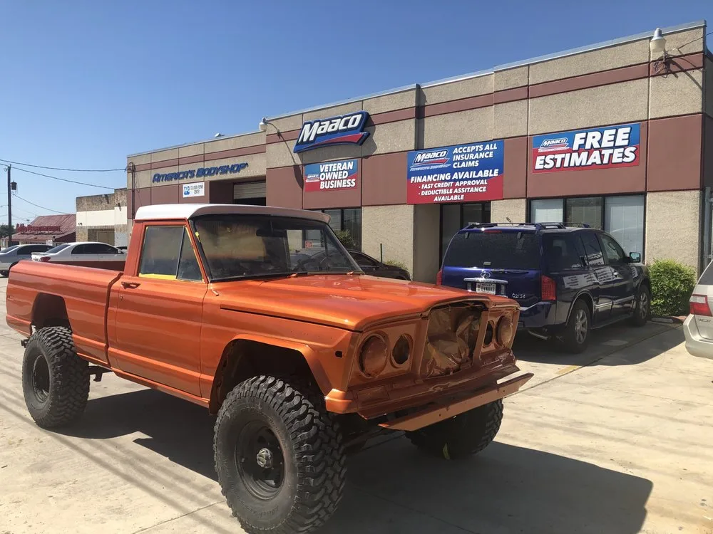 An orange pickup truck with its front grille and headlight assembly removed, parked in front of an auto body shop.